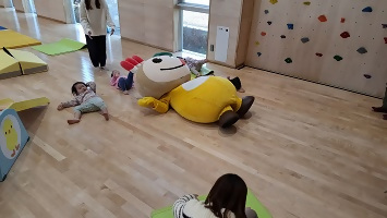 寝転んで広報の撮影をする子ども達とかまたんの写真