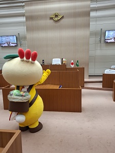 議場正面の鎌ケ谷市章を見上げるかまたんの写真