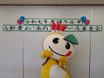 高齢者よい歯のコンクール審査会の貼り紙の前でポーズをとるかまたんの写真