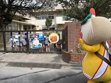 幼稚園の門からのぞき込む園児たちと、かまたんの写真